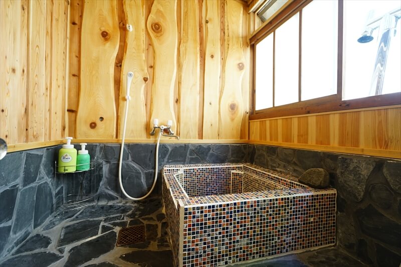 ▶室内の五右衛門風呂はシャワーもあり。壁面の木は地元の木材を使用。
